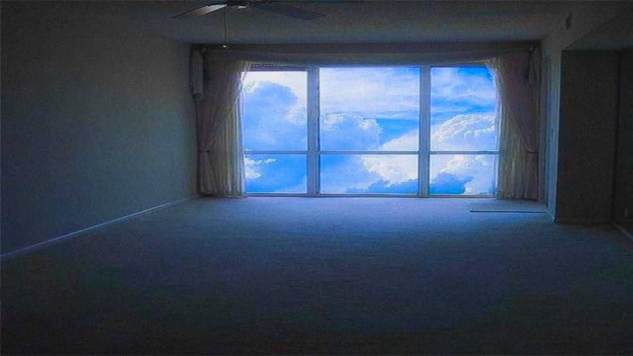 Sala com uma janela grande mostrando o céu claro e com nuvens